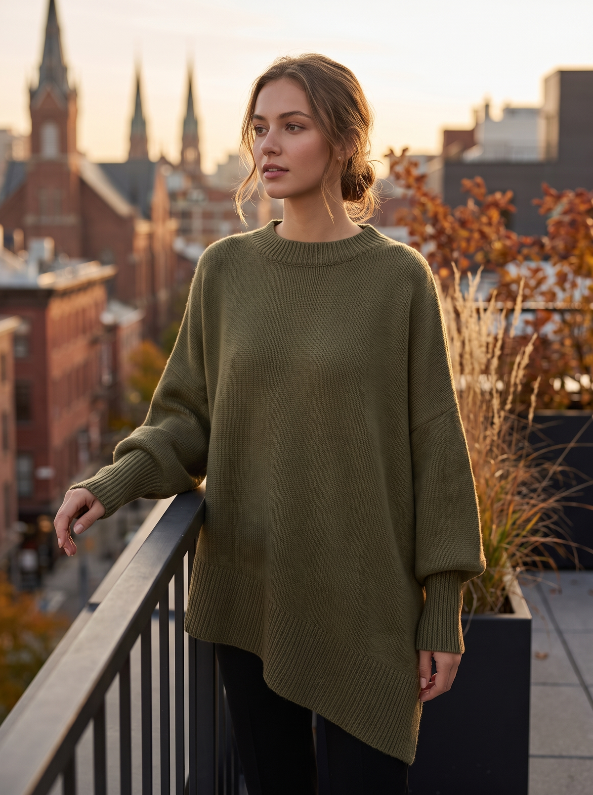Aurelia olive green merino wool asymmetric sweater worn by a model on a city rooftop terrace in autumn