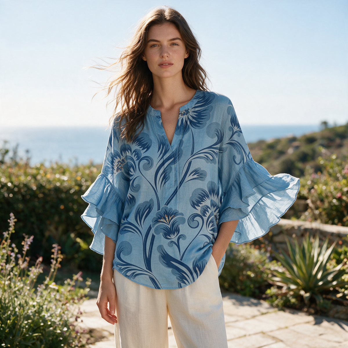 Model wearing the light blue Janessa blouse on a coastal garden terrace