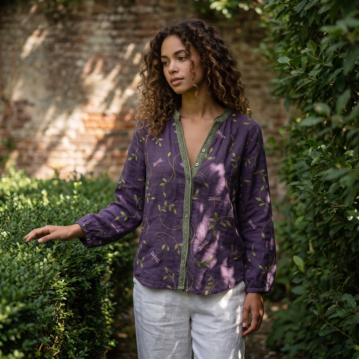 Woman in a walled garden wearing the Purple embroidered blouse
