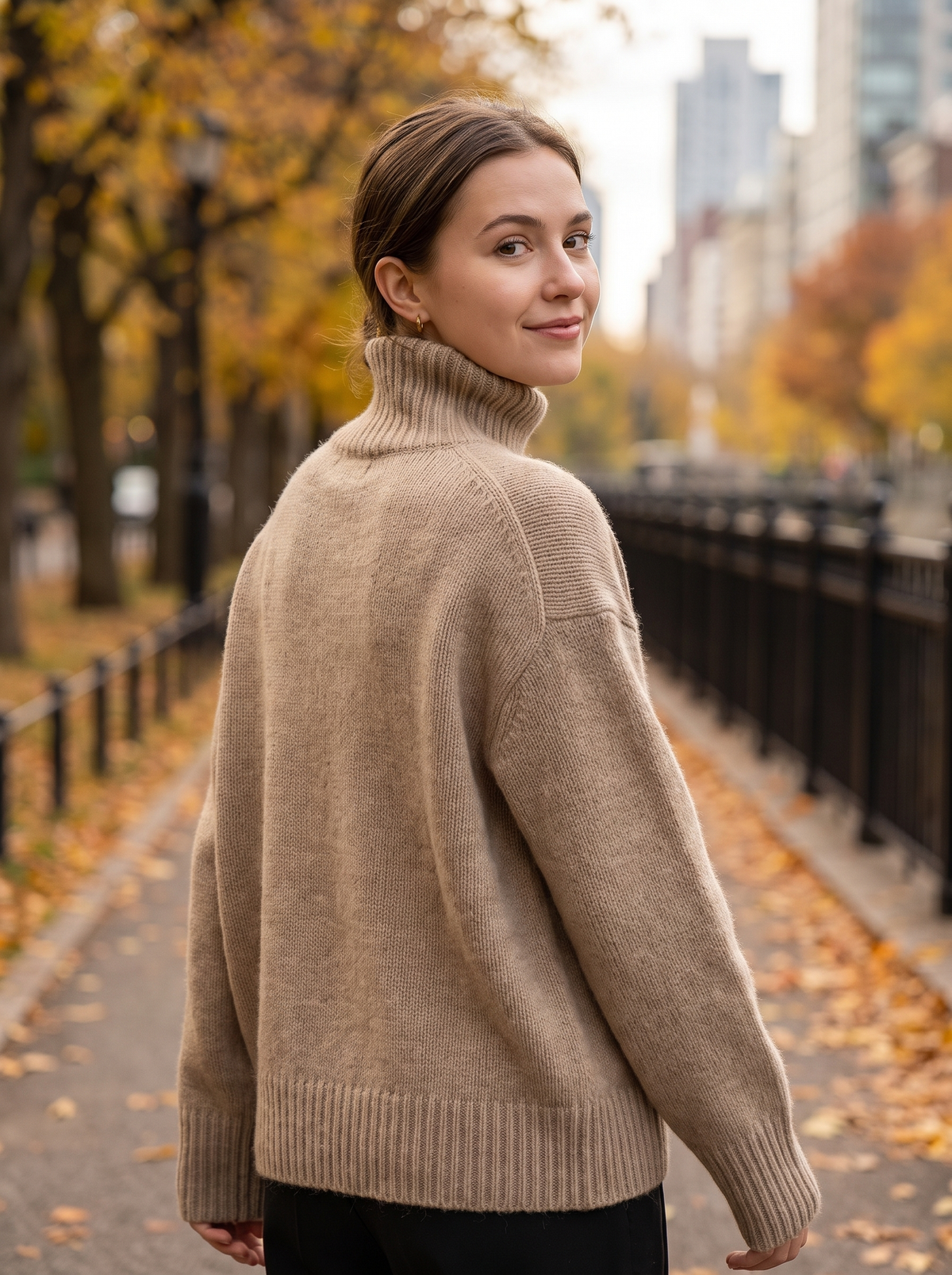 Back view of the Cosima khaki cashmere roll neck sweater on an autumn city park path
