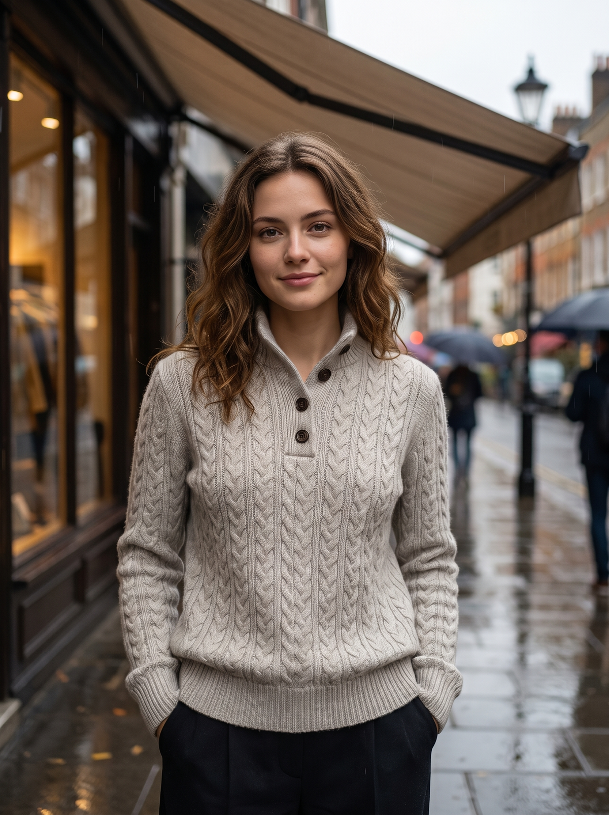 Lavinia grey cable knit sweater worn by a model under a shop awning on a rainy street in autumn