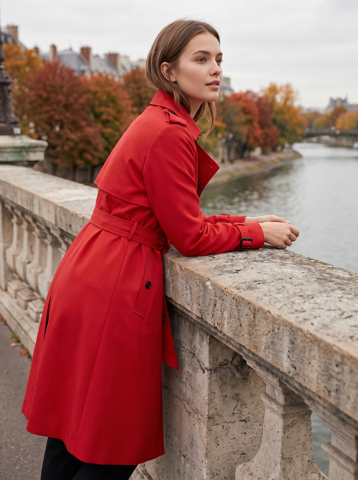 Aveline red double breasted trench coat worn by a model on a city bridge in autumn