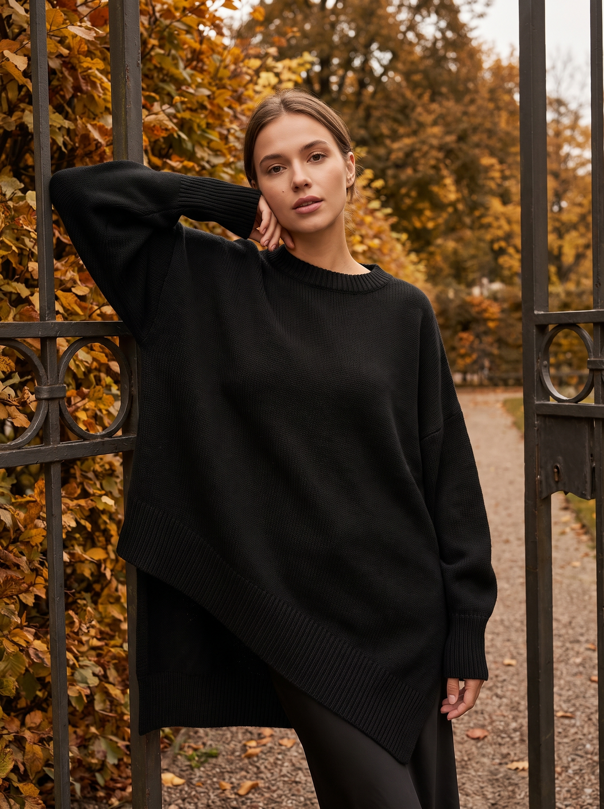 Aurelia black merino wool asymmetric sweater worn by a model at a park gate in autumn