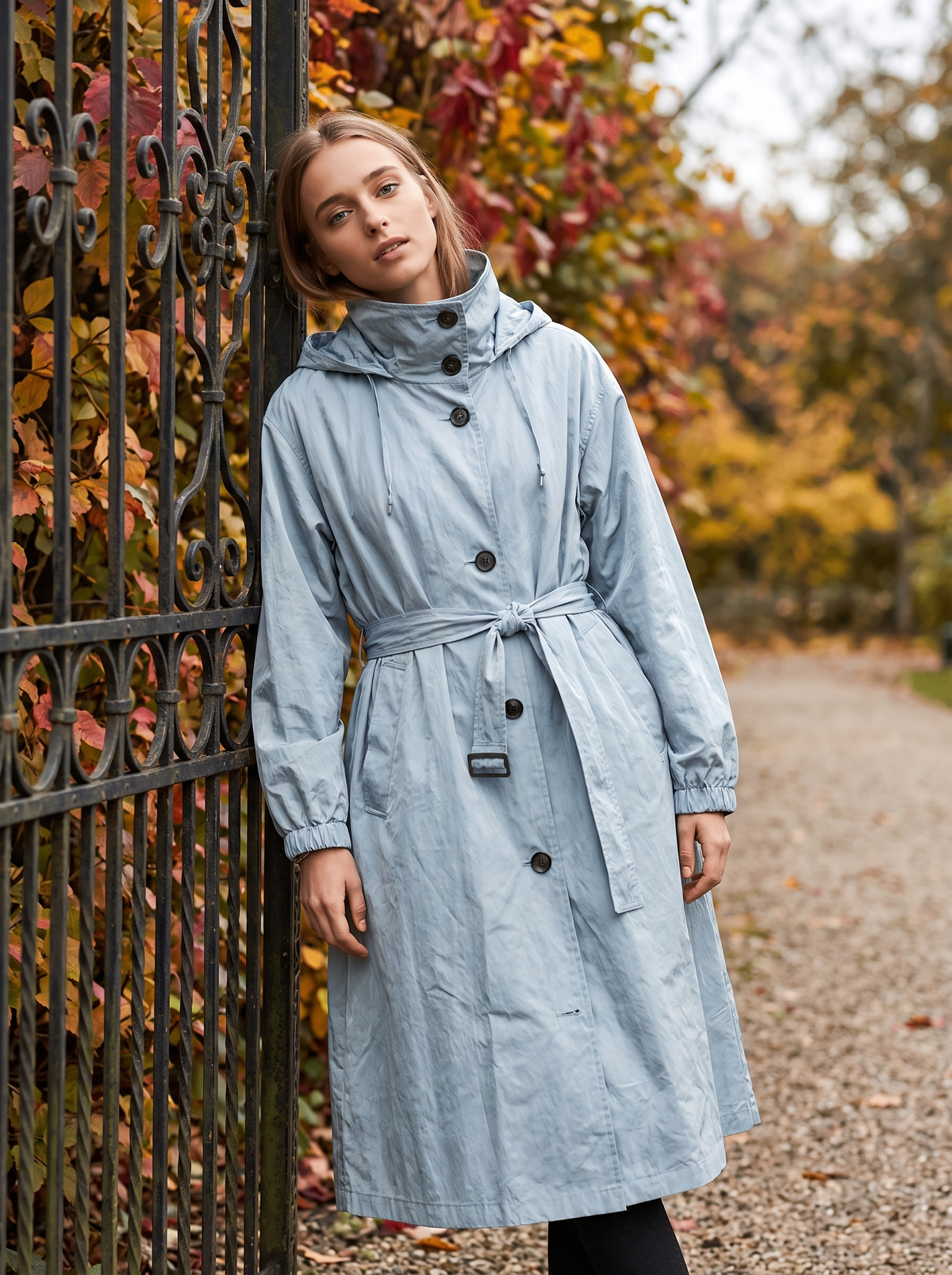 Mirabelle light blue oversized trench coat worn by a model at a park gate in autumn