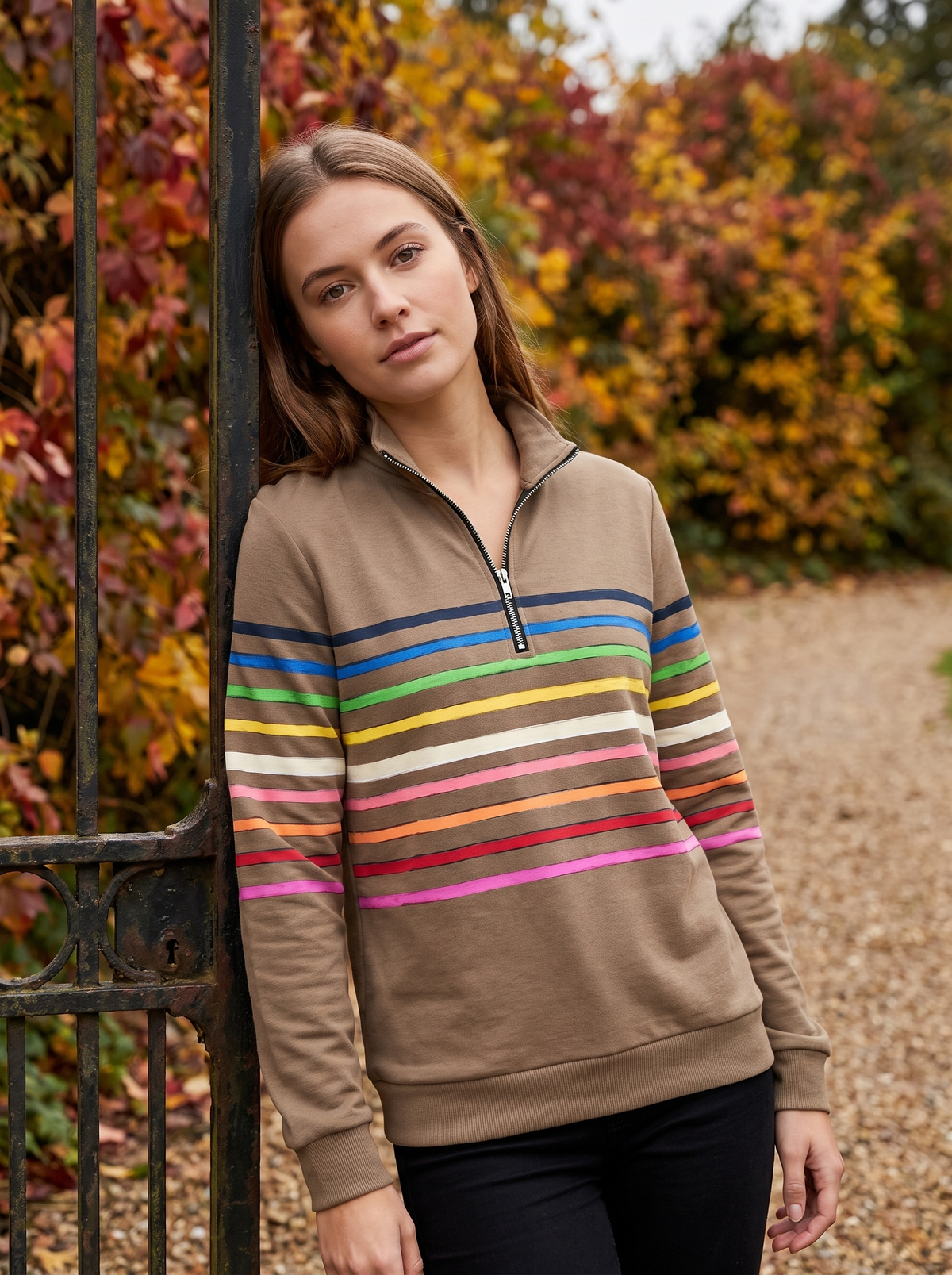 Zephyrine khaki striped half zip sweatshirt worn by a model at a park gate in autumn