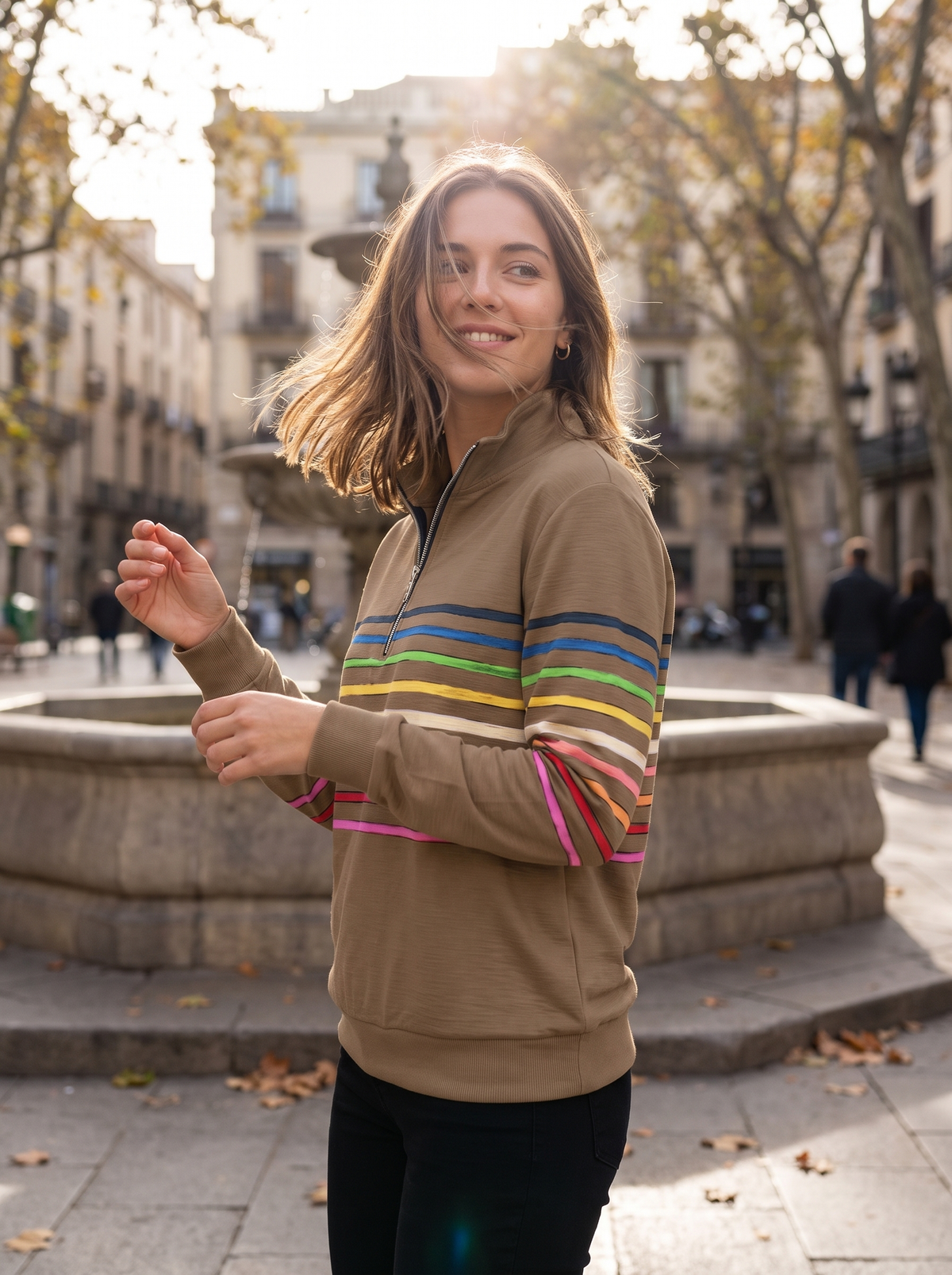 Zephyrine khaki striped half zip sweatshirt worn by a model by a fountain in a city square in autumn