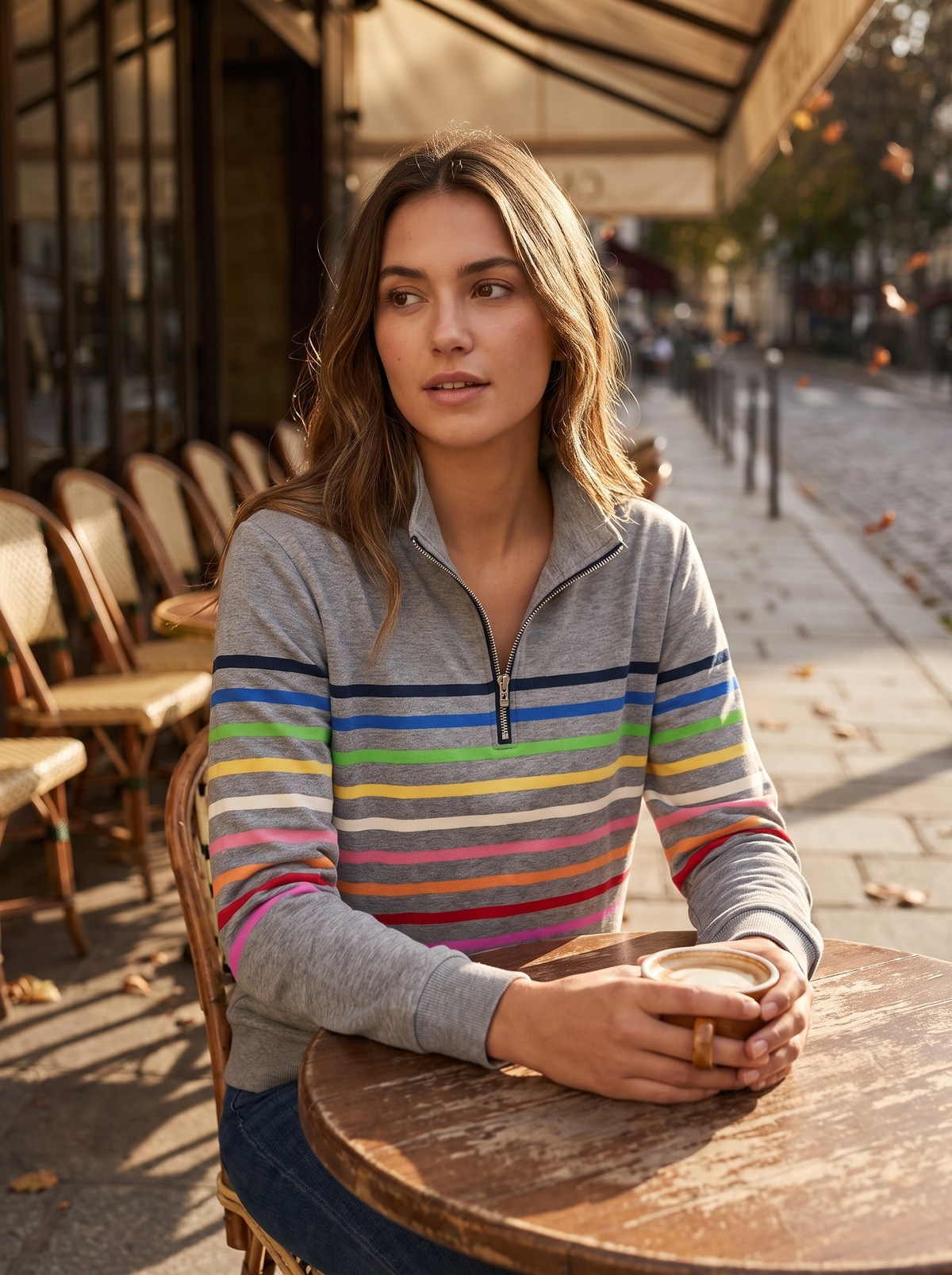 Zephyrine grey striped half zip sweatshirt worn by a model at an outdoor city cafe in autumn