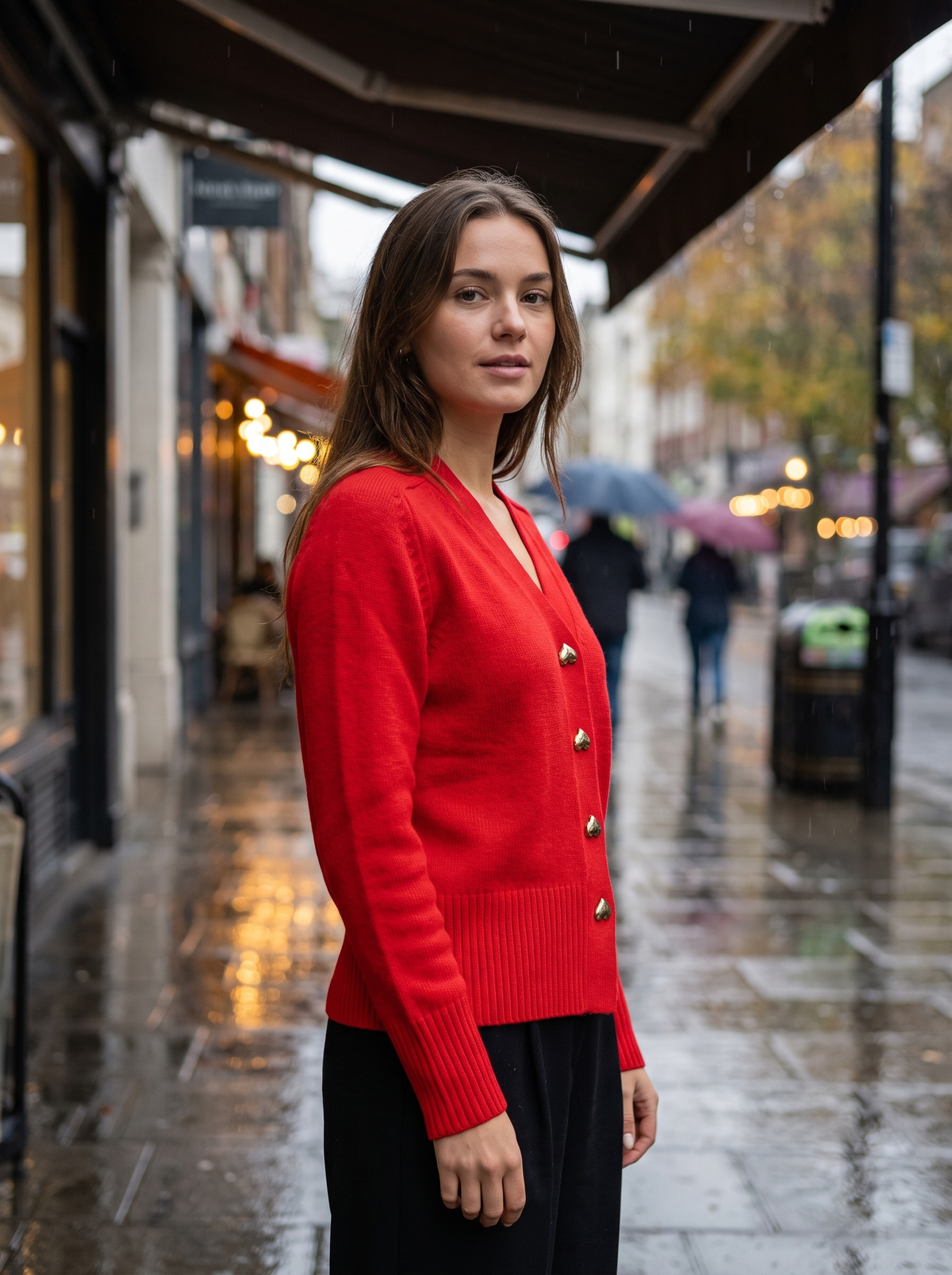 Yolande red ribbed knit cardigan worn by a model under a shop awning in the rain in autumn