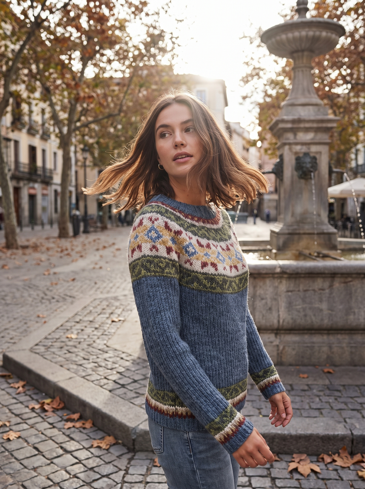 Vespera grey star crew neck knit sweater worn by a model by a fountain in a city square in autumn
