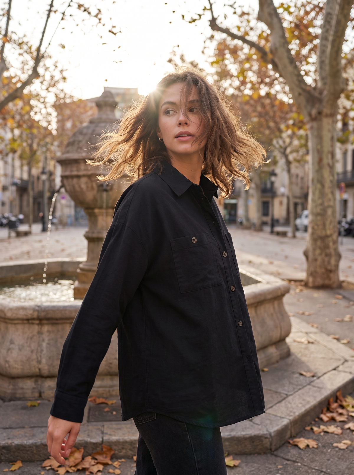 Linnea black cotton shirt jacket worn by a model by a fountain in a city square in autumn