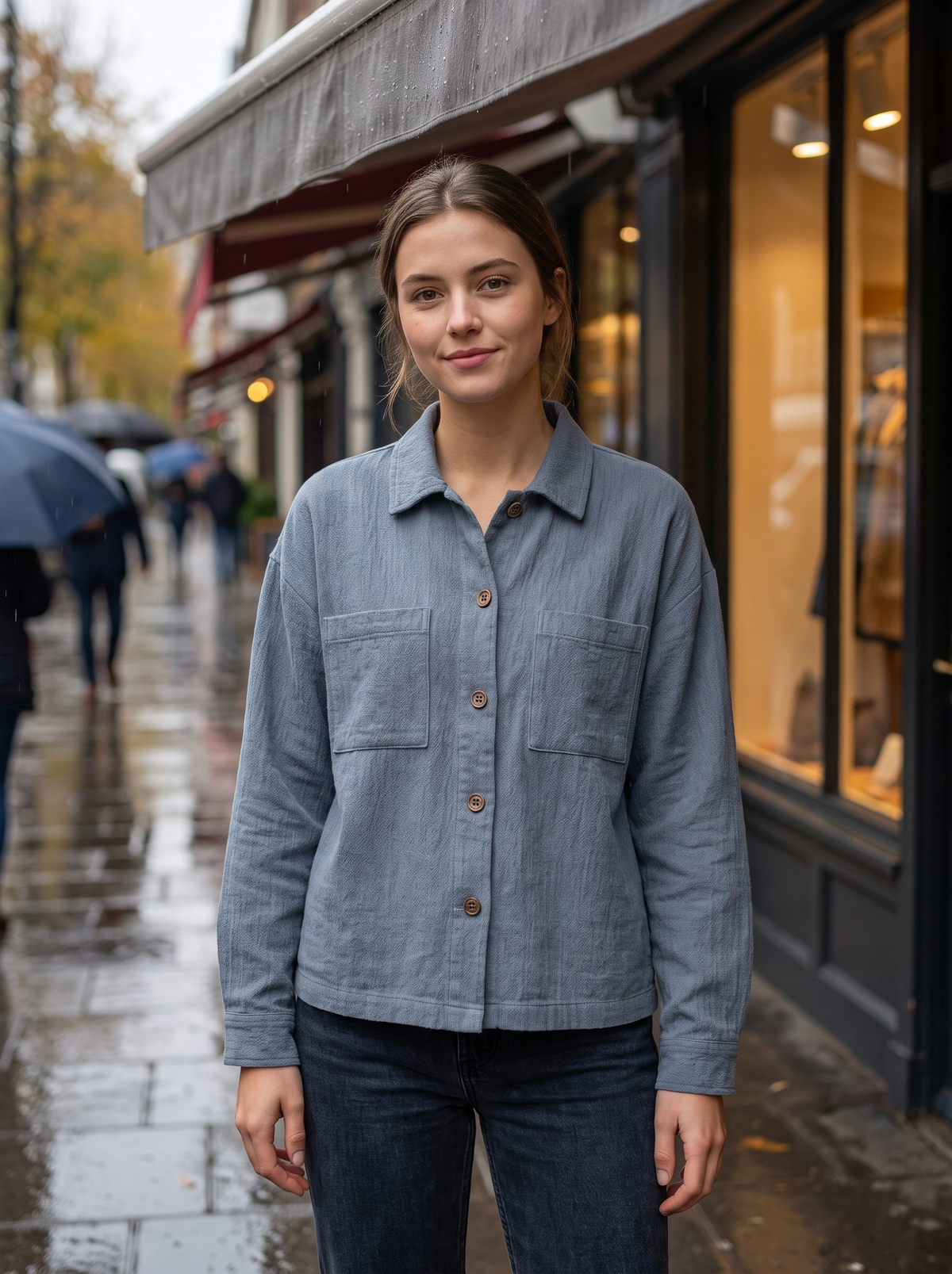 Linnea blue grey cotton shirt jacket worn by a model under a shop awning in the rain in autumn