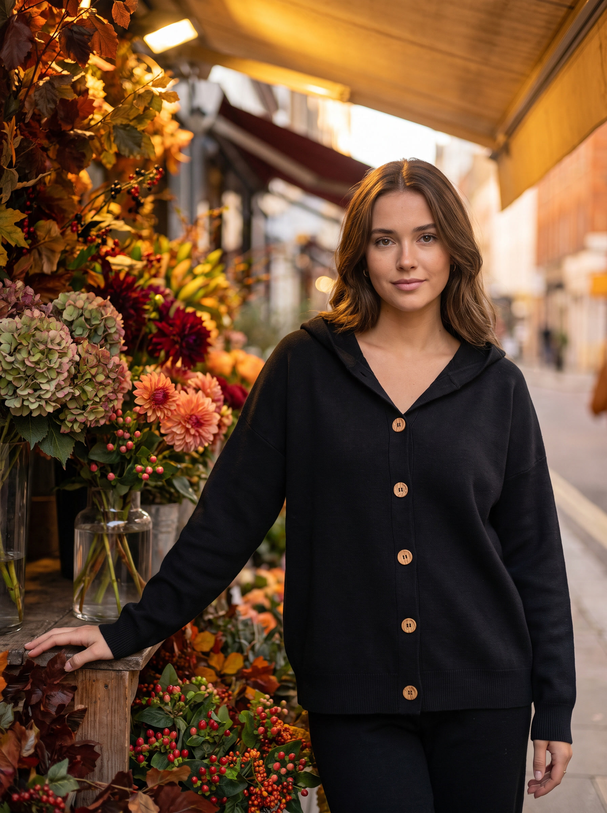 Bellamy black hooded cardigan worn by a model beside a city flower stall in autumn